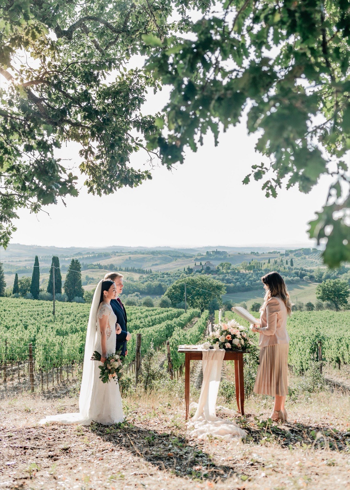 Bride and groom exchanging vows under an oak tree overlooking a Tuscan vineyard