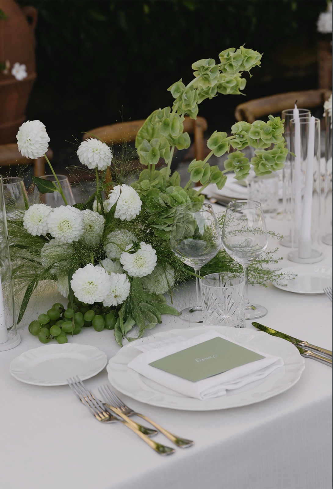 Elegant table setting with white pompom dahlias, green bells-of-Ireland, grapes and crystal glassware